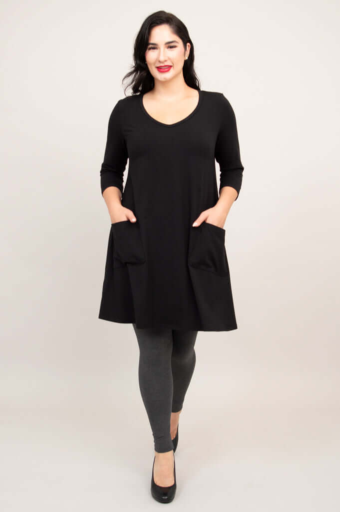 Model walking forward in black A-line tunic dress with hands in pockets