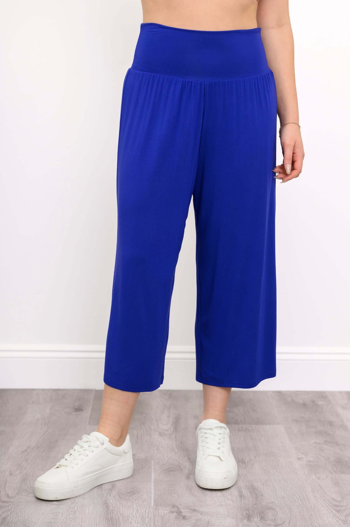 Front view of blue cropped capri pants with wide waistband and white sneakers