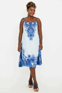 Woman wearing a light blue knee-length dress with blue tropical print and tie shoulder strap, front view