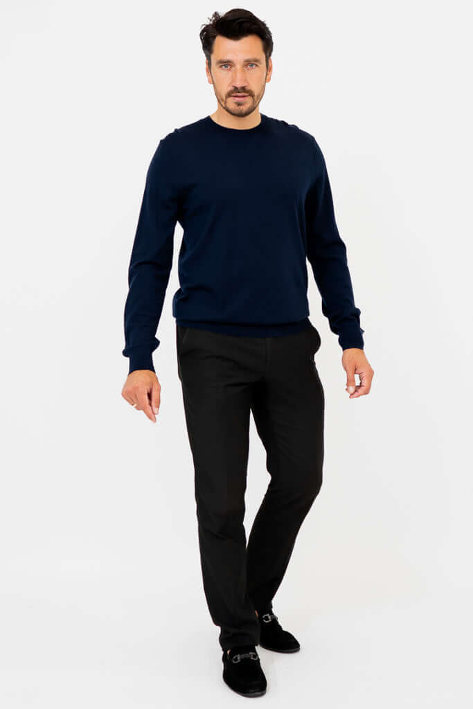 Man in navy merino wool sweater, walking toward camera in black pants