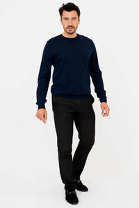 Man in navy merino wool sweater, walking toward camera in black pants