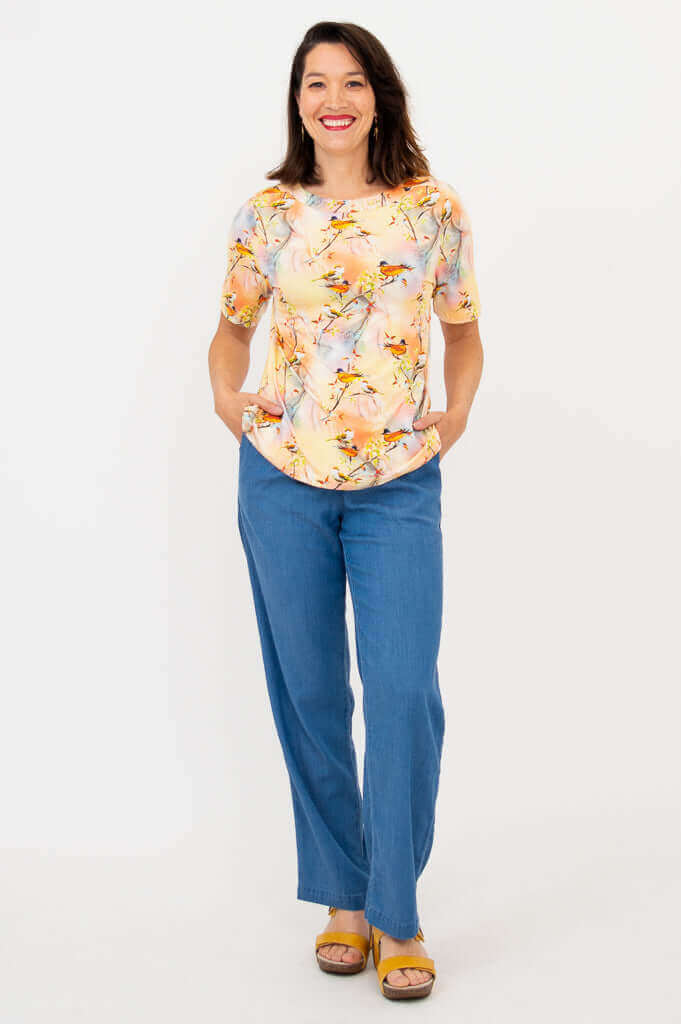 Full body view of woman in a bird print short sleeve tee and blue jeans, standing