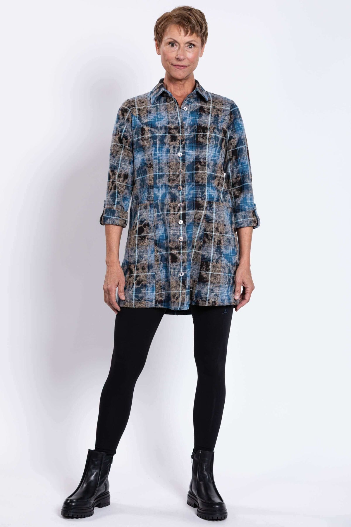 Full body front view of woman in blue plaid tunic and black leggings, facing forward