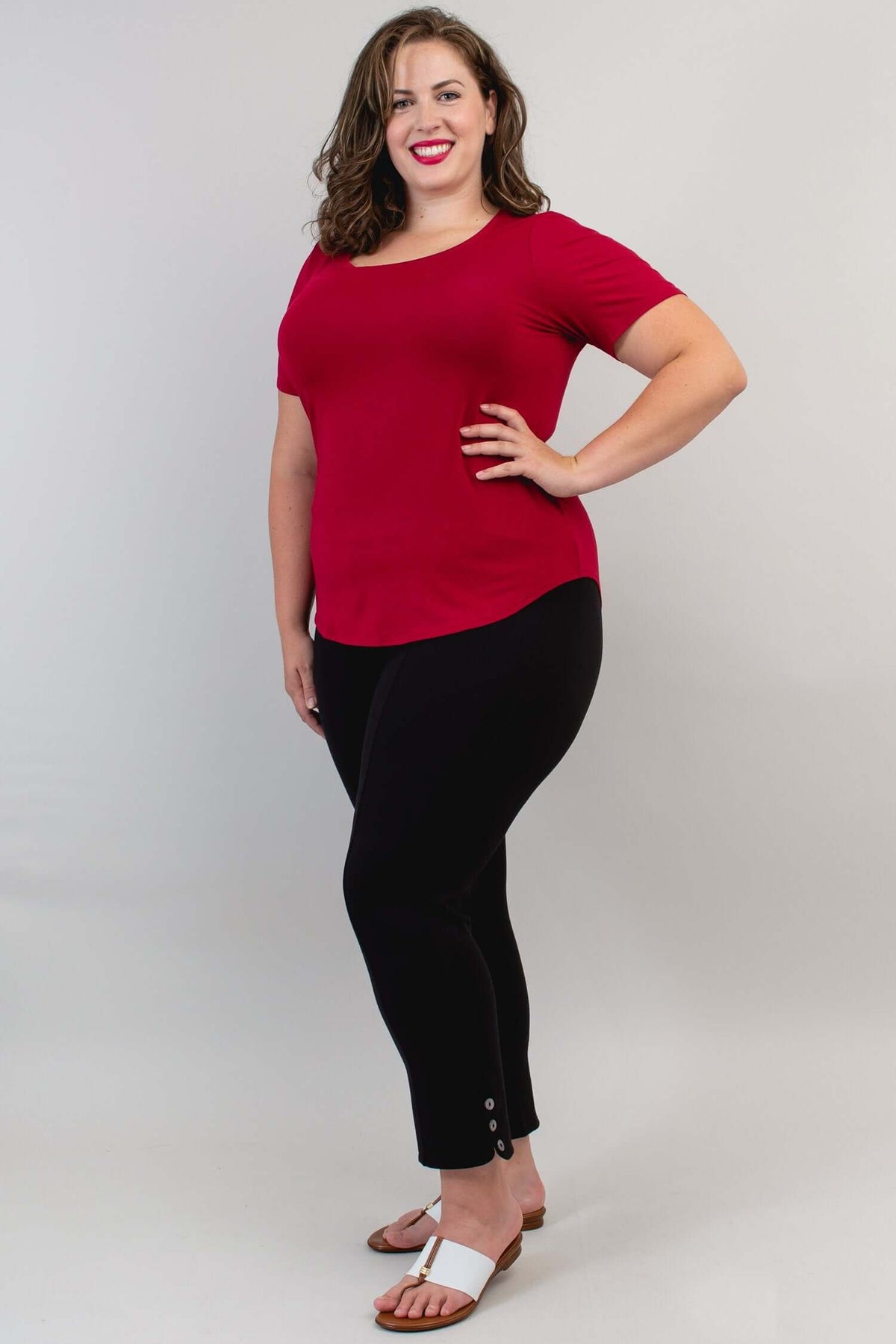 Woman in a crimson scoop neck tee and black pants, hand on hip, full body