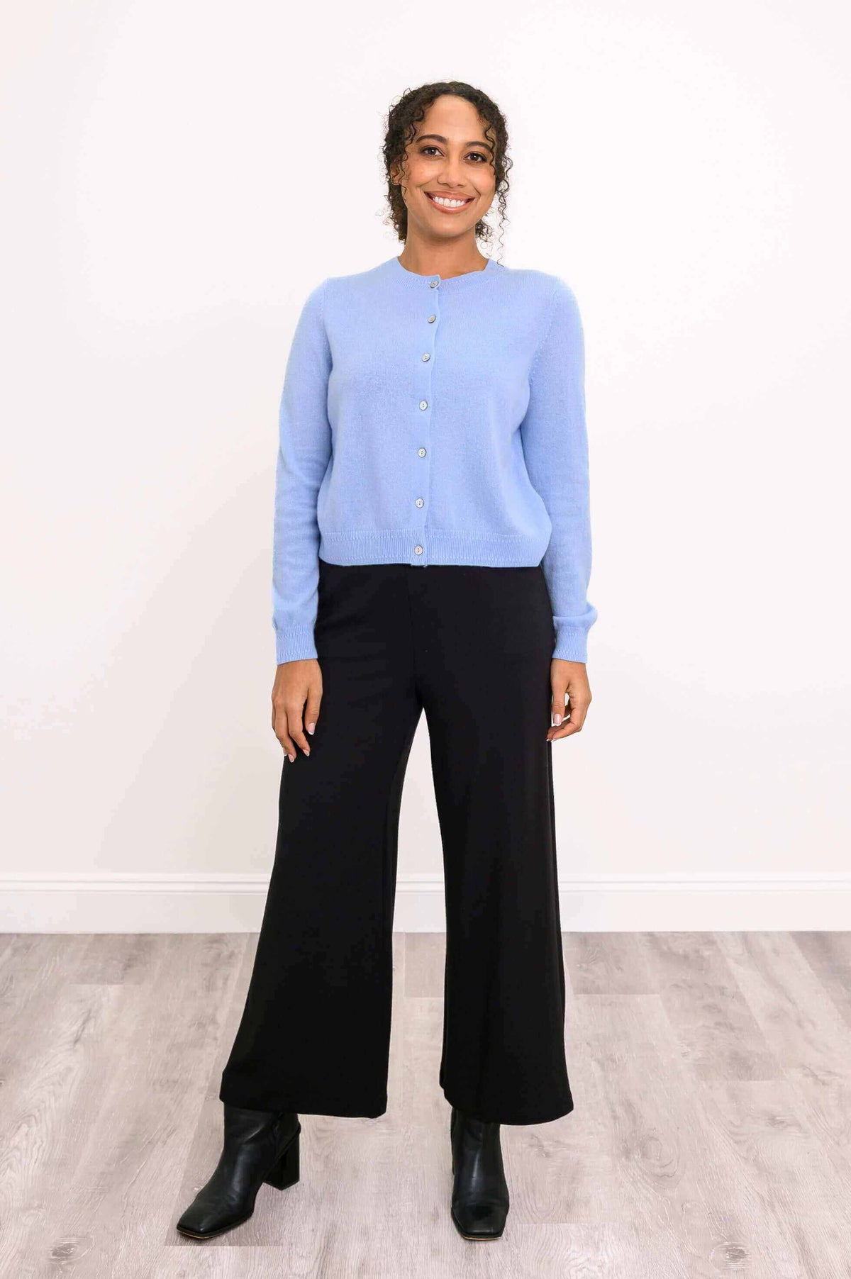 Full body view of a woman in a blue cardigan and black wide-leg pants with boots