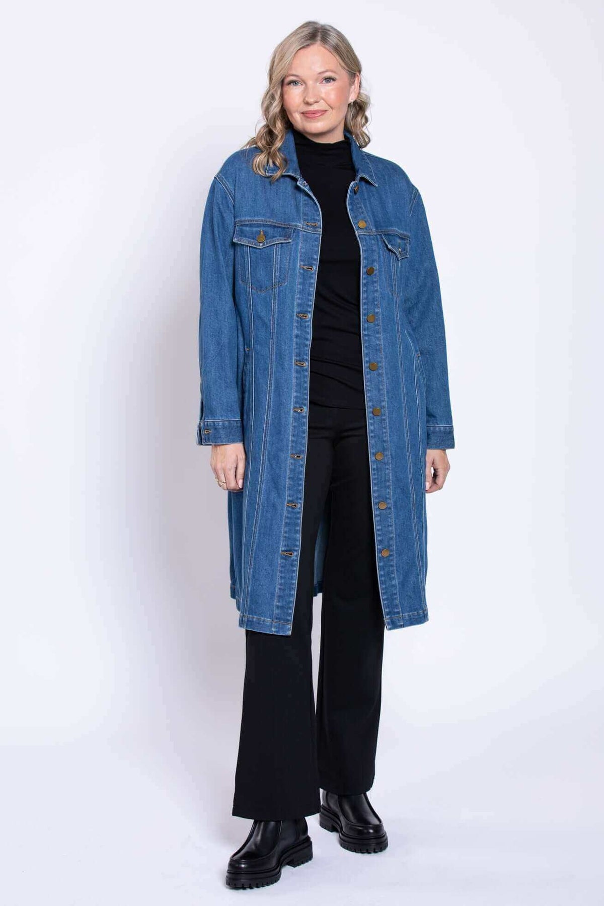 Full body view of a woman wearing a black inner outfit paired with a long blue denim duster coat.