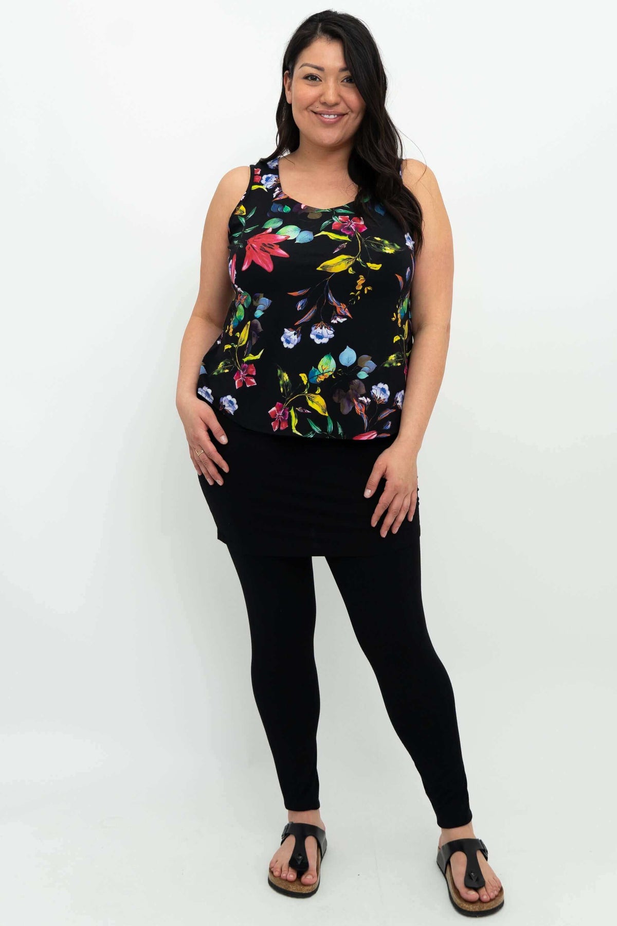 Full body view of woman in black floral tank top, black skirt, and leggings