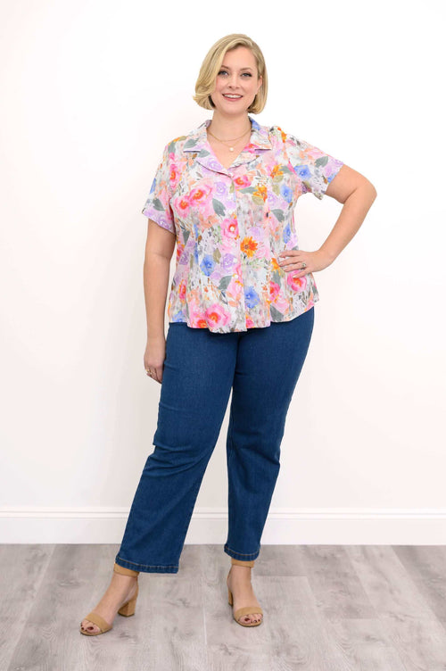 Full body view of a woman modeling pink floral button-up blouse and denim pants