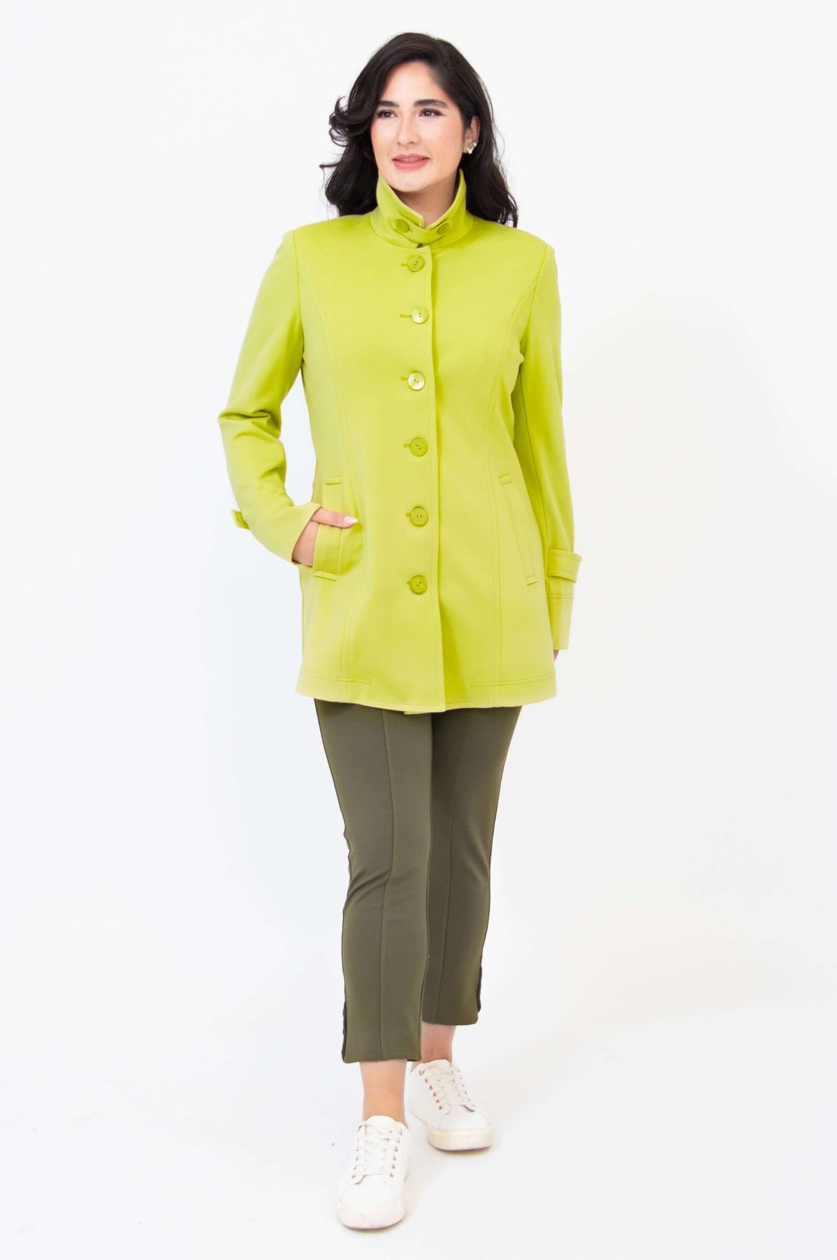 Woman standing, wearing lime green jacket and olive pants, hand in pocket