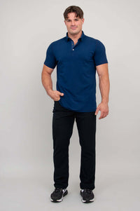 Man in navy polo shirt, hand in pocket, standing full height facing forward