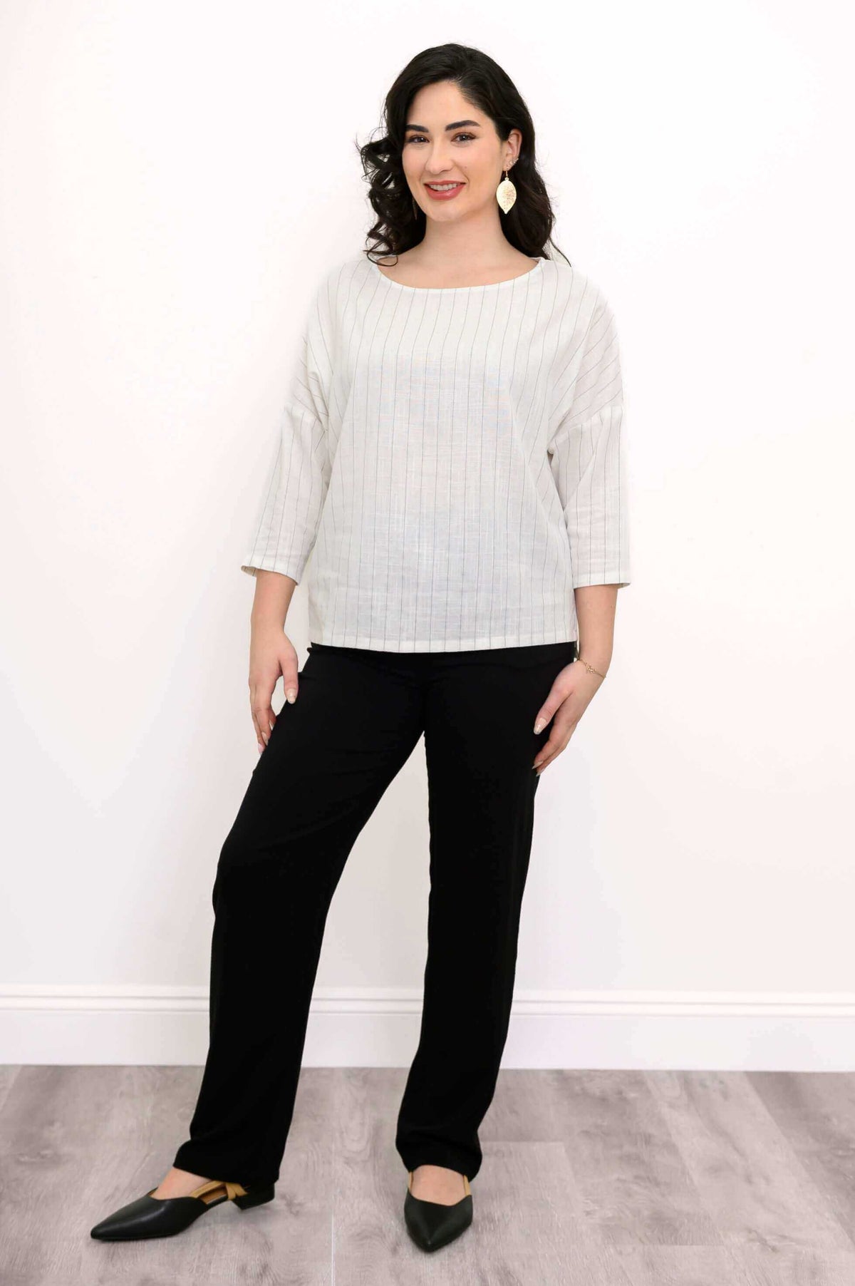 Woman standing in white pinstripe top and black pants with pointed black flats
