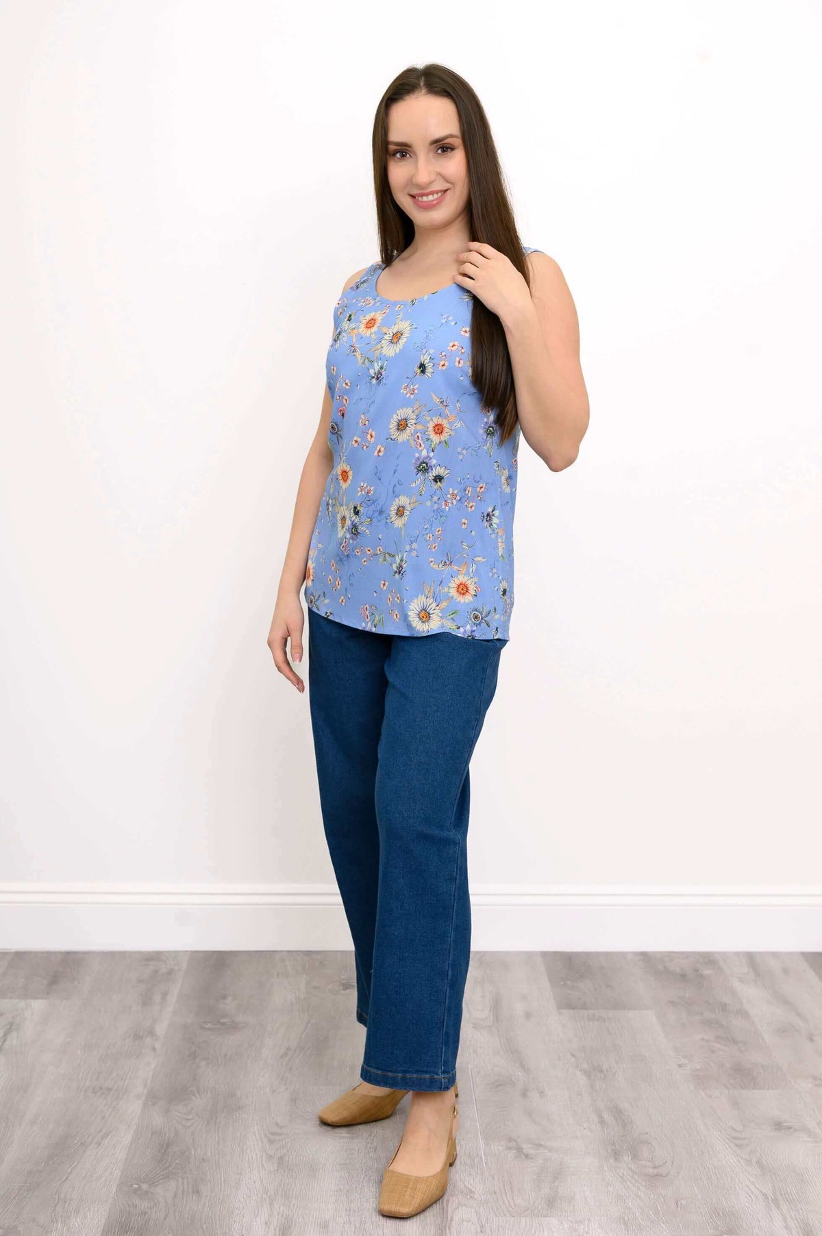 Woman standing in blue floral tank top, blue jeans, and tan shoes