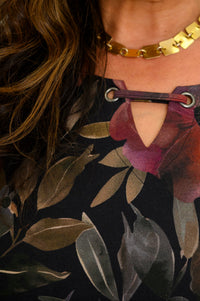 Close-up of a women's colorful floral knit top, highlighting the notched keyhole neckline and gold necklace.