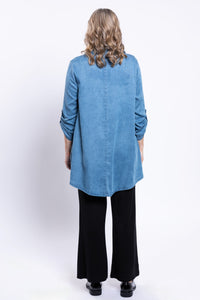 Back view of woman wearing flowy tencel denim tunic with black pants and black shoes