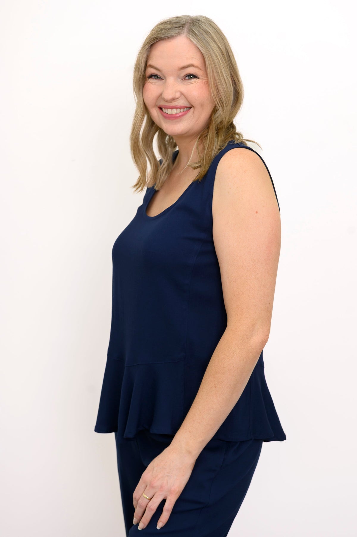 Side view of woman wearing a navy blue sleeveless top and navy blue pants on a white background