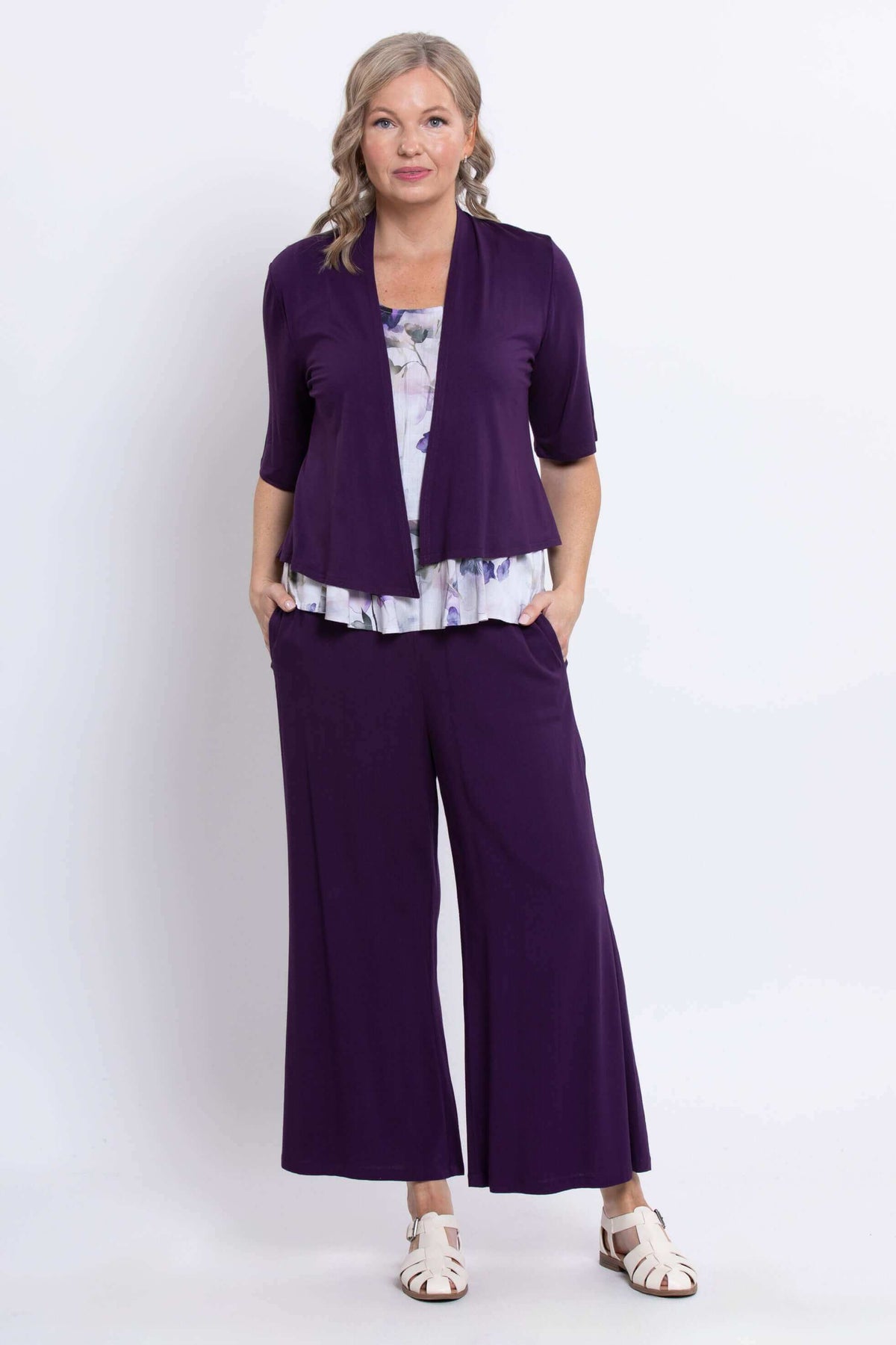 Model wearing purple watercolor peplum top underneath purple open cardigan and matching pants