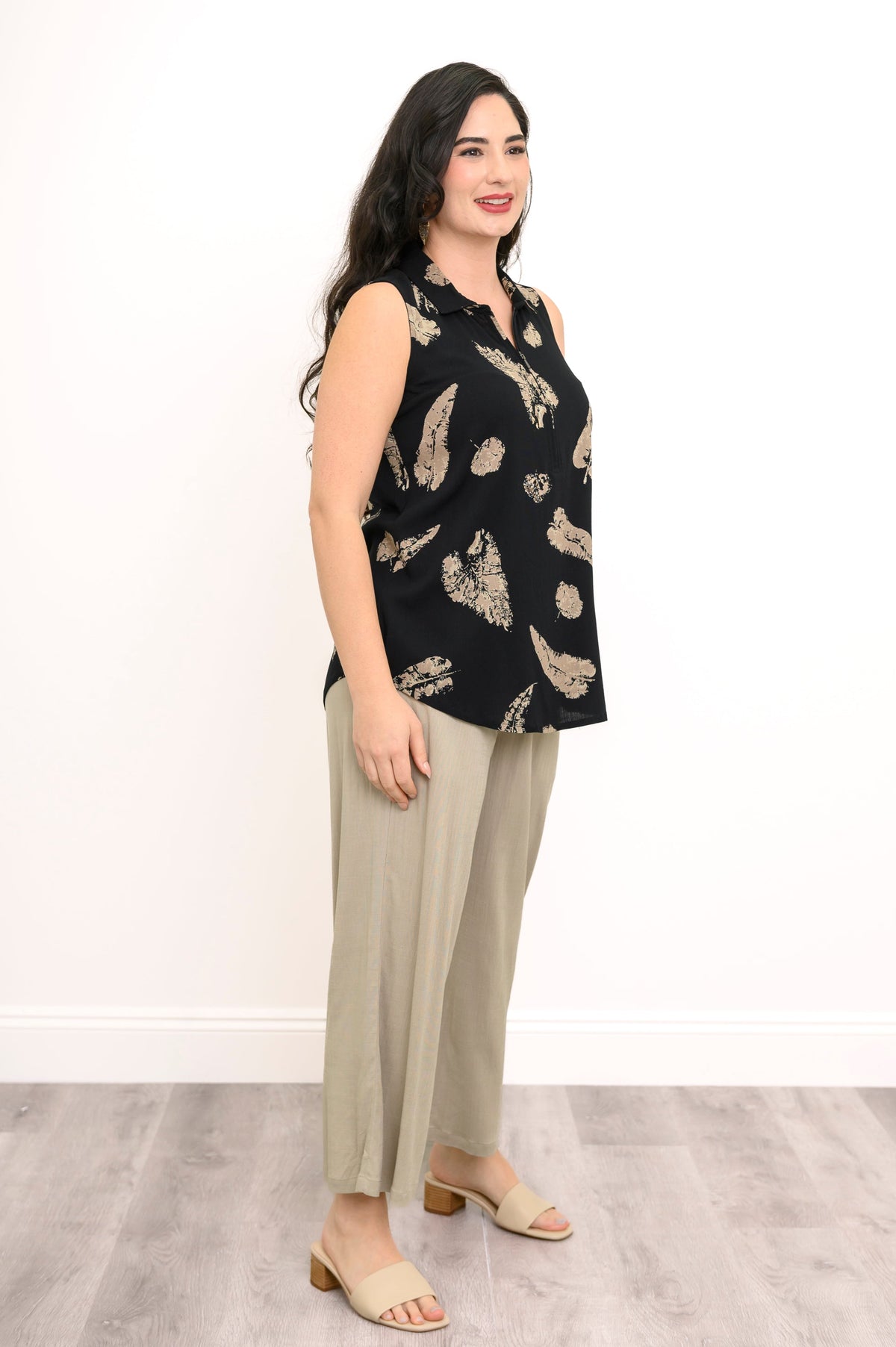 Full body angled view of woman wearing a 1/4 zip top with leaf print and beige pants