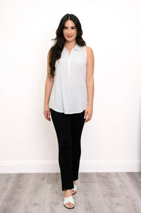 full body view of woman modeling a white sleeveless top, black pants, and white sandals