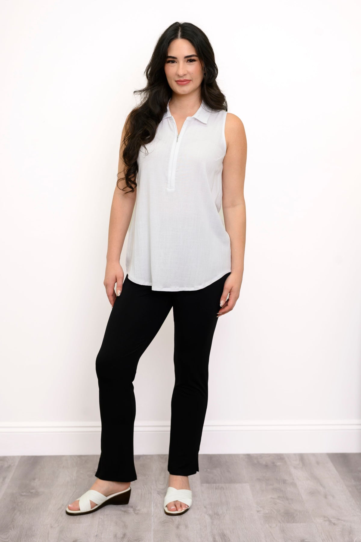 full body front view of woman wearing white zippered tank top, slim black pants, and white shoes