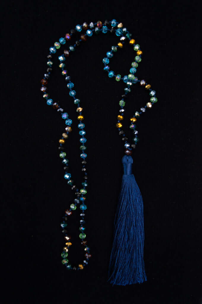 Iridescent multi-color beaded necklace with long blue tassel on black background