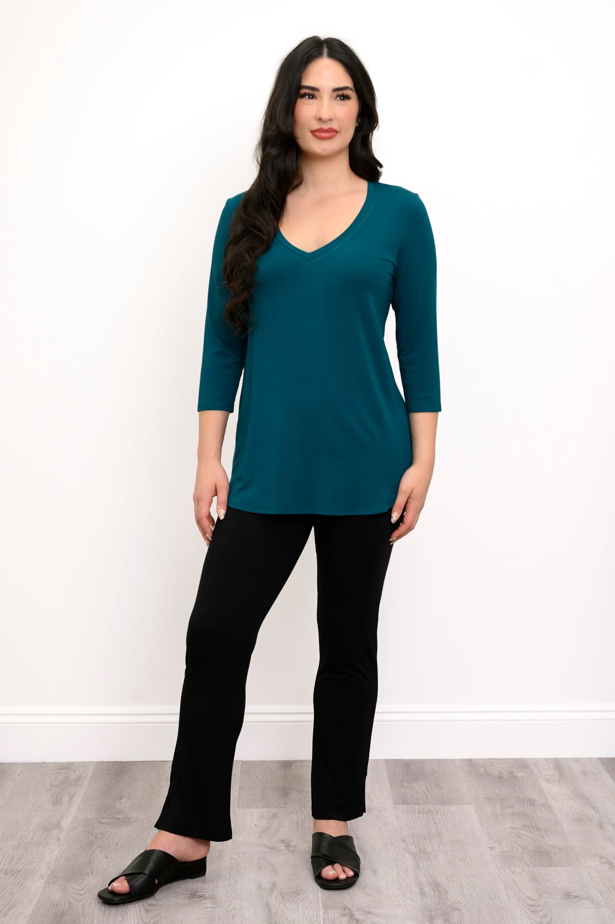full body front view of woman wearing a teal 3/4 sleeve top, slim black pants, and black sandals