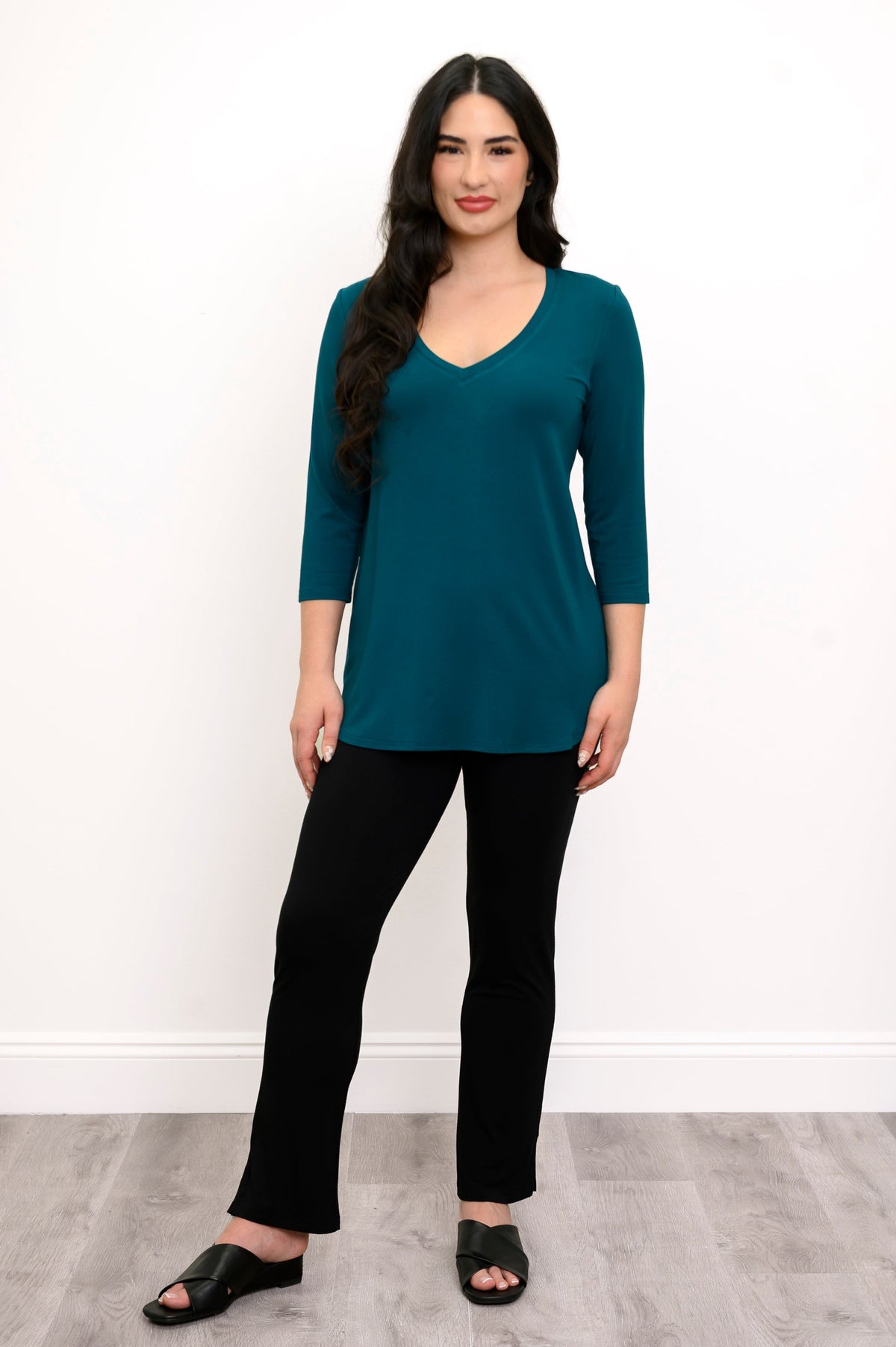 full body view of woman wearing v-neck teal top with 3/4 sleeves, black pants, and black sandals