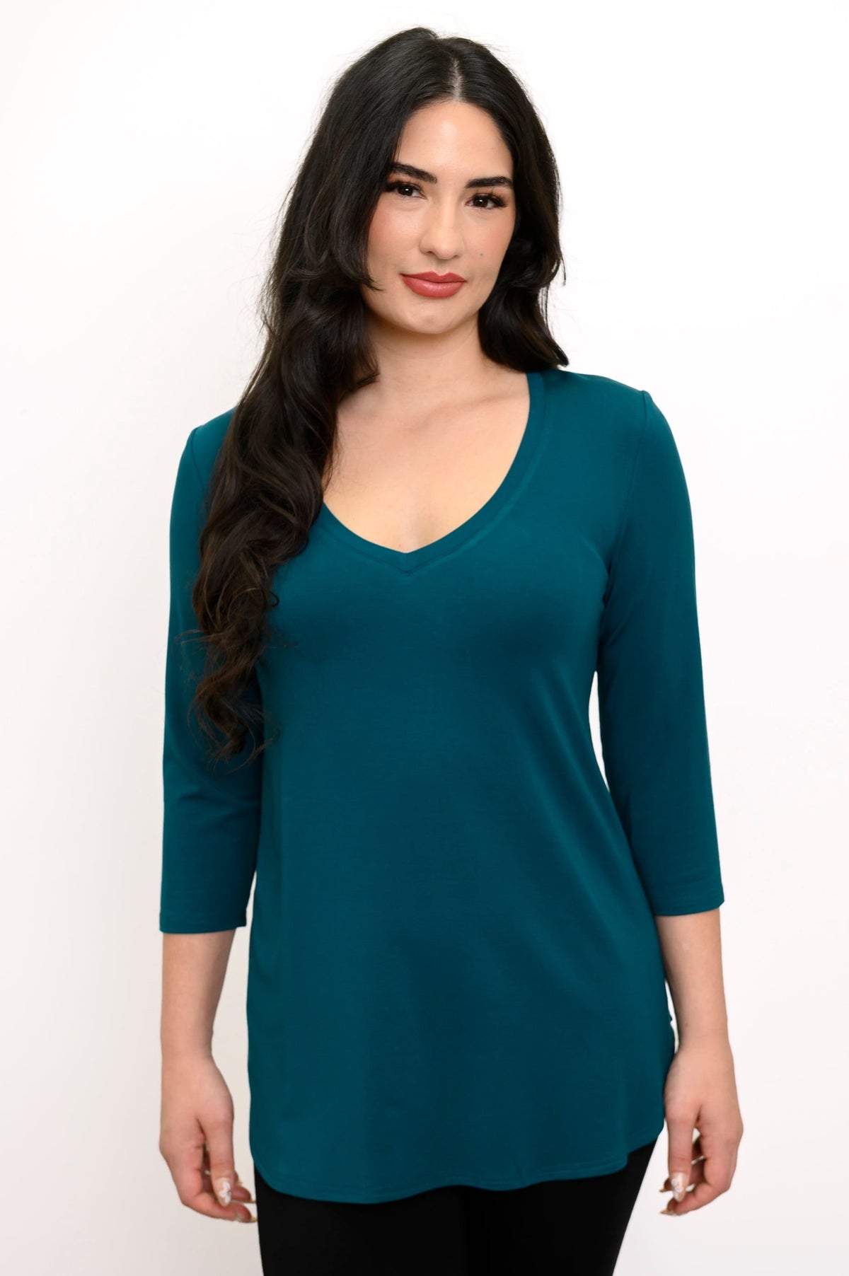 Close up front view of woman smiling wearing a teal colored v-neck top and black pants