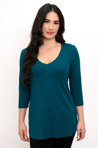 Close up front view of woman smiling wearing a teal colored v-neck top and black pants