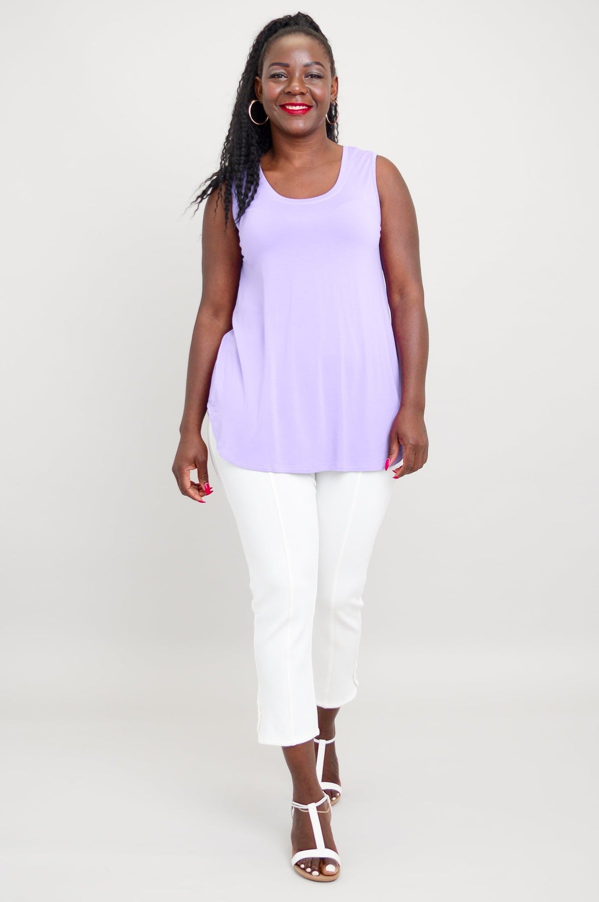 Front view of woman smiling in lavender round neck tank, white pants, and white sandals
