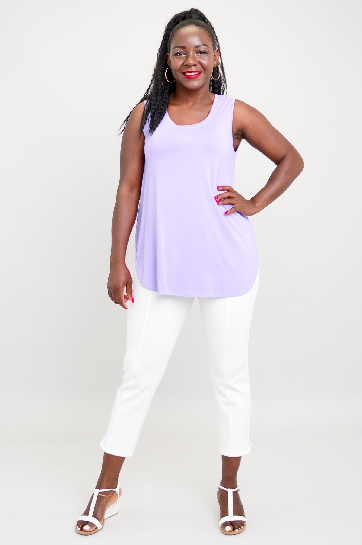 Woman standing with her hand on her hip in a relaxed fit lavender tank, white pixie pants, and white sandals