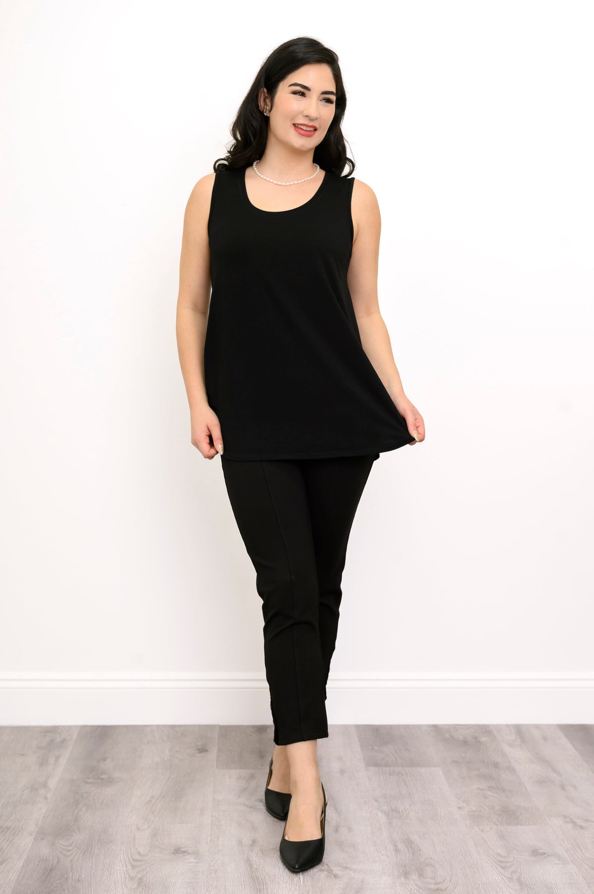 Woman wearing a black sleeveless top and black pants against a white background, front view