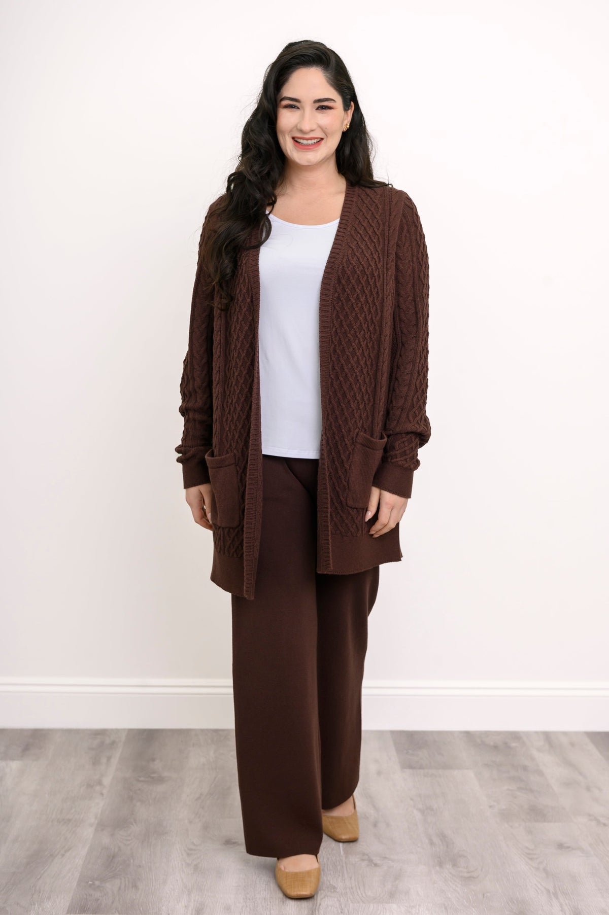 Layered autumn outfit featuring dark brown knit pants, a white inner top, and an earthy brown outer cardigan.