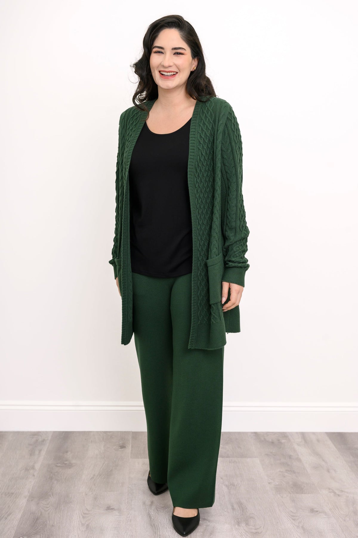 Model wearing a dark forest green cotton viscose long knit cardigan sweater with pockets.