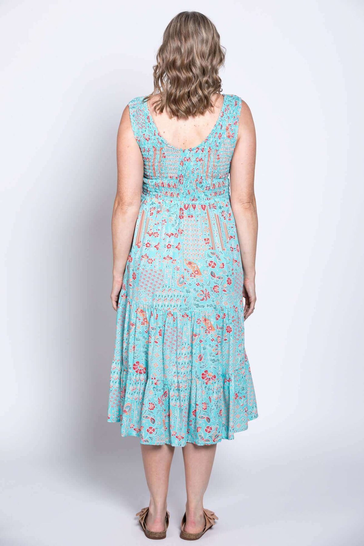 Back view of woman in blue tiered sleeveless dress with red floral print