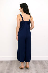 Woman wearing a navy blue jumpsuit and beige sandals against a white background, back view