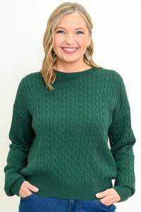 Front view of a female model wearing a green sweater with denim pants, against a white backdrop