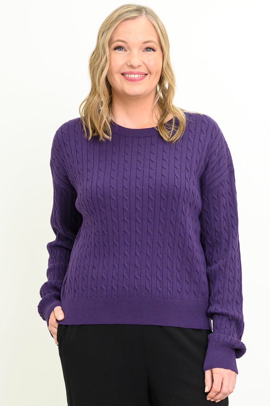 Front view of a female model wearing a purple sweater with black pants, against a white backdrop