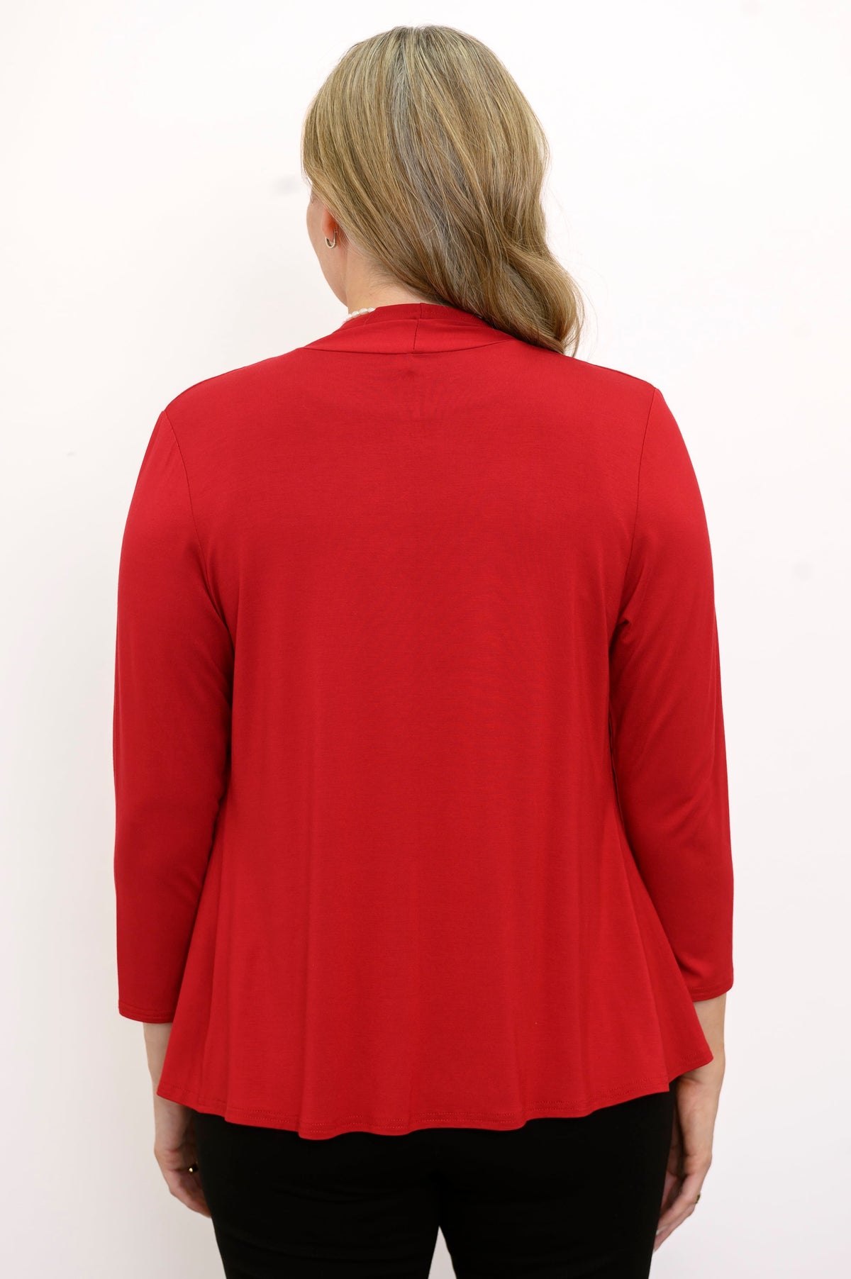Back view of woman wearing a red cardigan, black top, and black pants on a white background