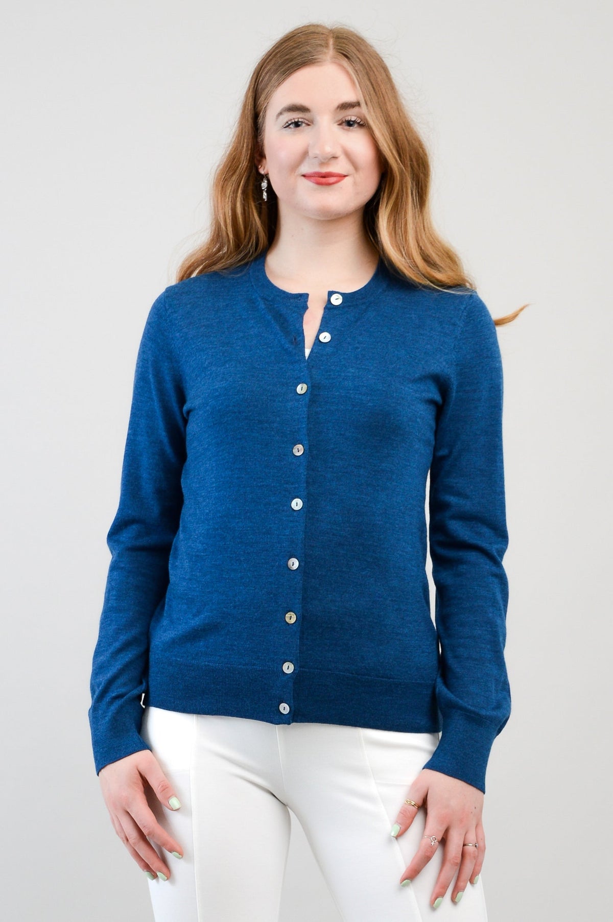 Close up front view of a woman wearing a blue merino wool crewneck cardigan with small buttons.
