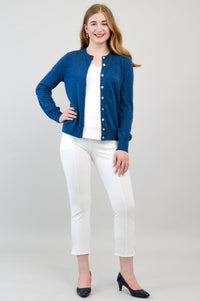 Full body image of a woman showcasing a bright blue crewneck fine knit cardigan and white pants.
