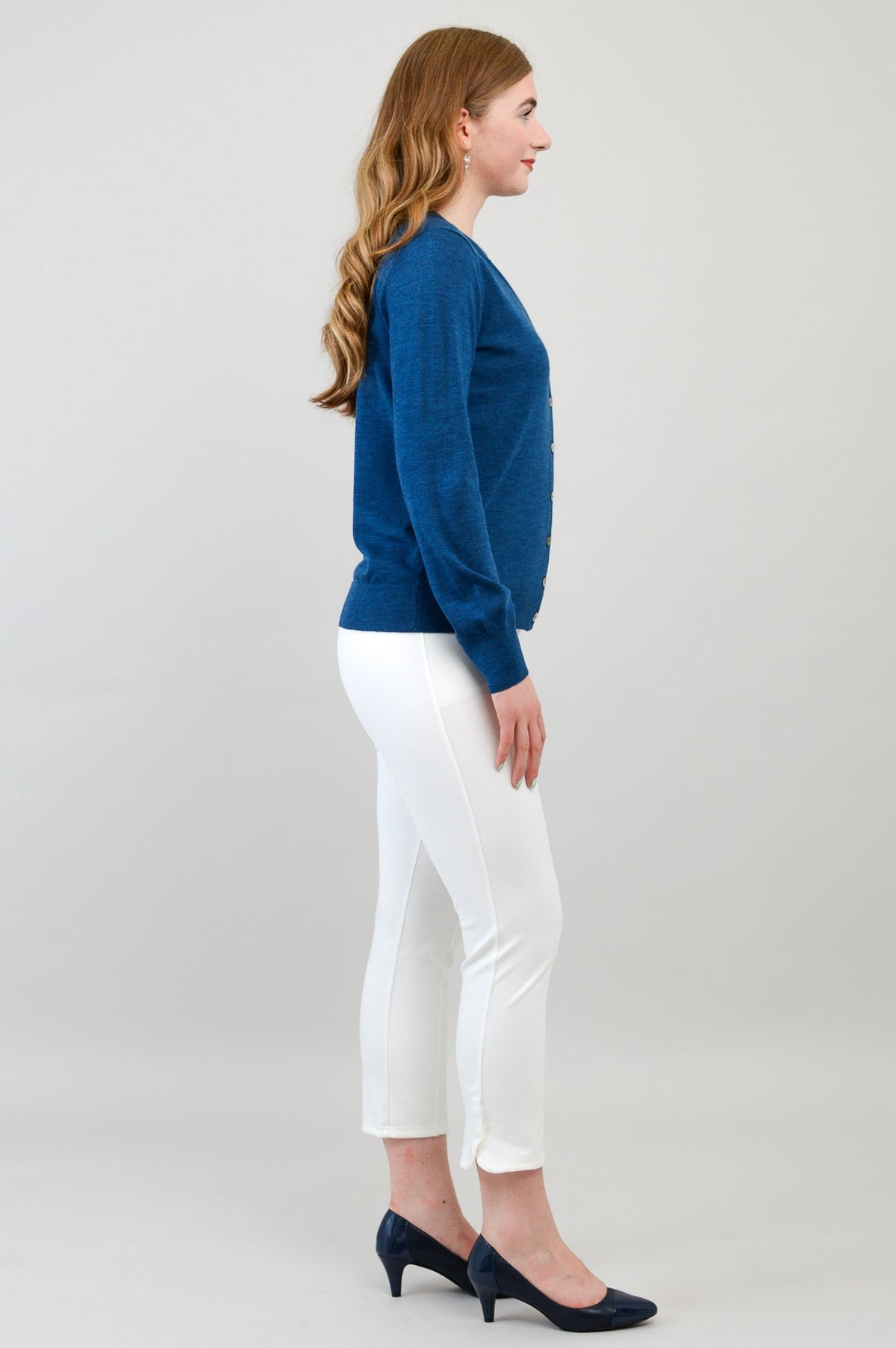 Full length shot of a woman wearing a blue merino wool button up cardigan layered with white pants