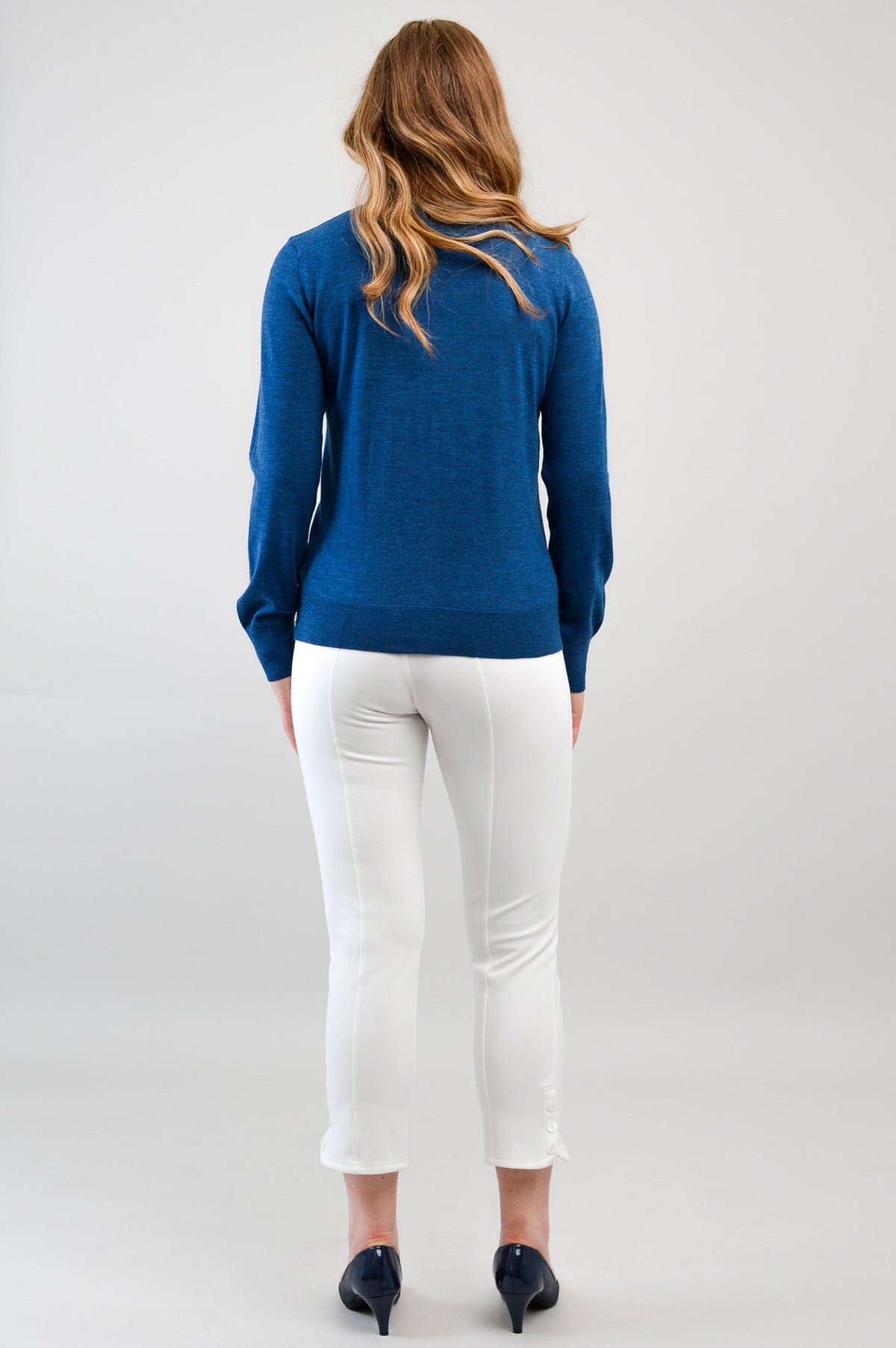 Back view of a woman wearing a blue merino wool crewneck cardigan showing ribbed hem construction.