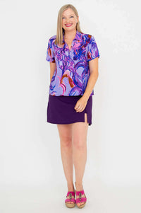 Model facing forward in a purple abstract print short sleeve blouse and purple skirt