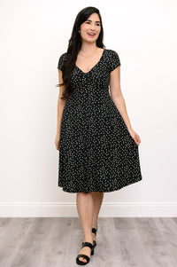 Full body shot of woman smiling and looking away while wearing a polka dot dress and black sandals