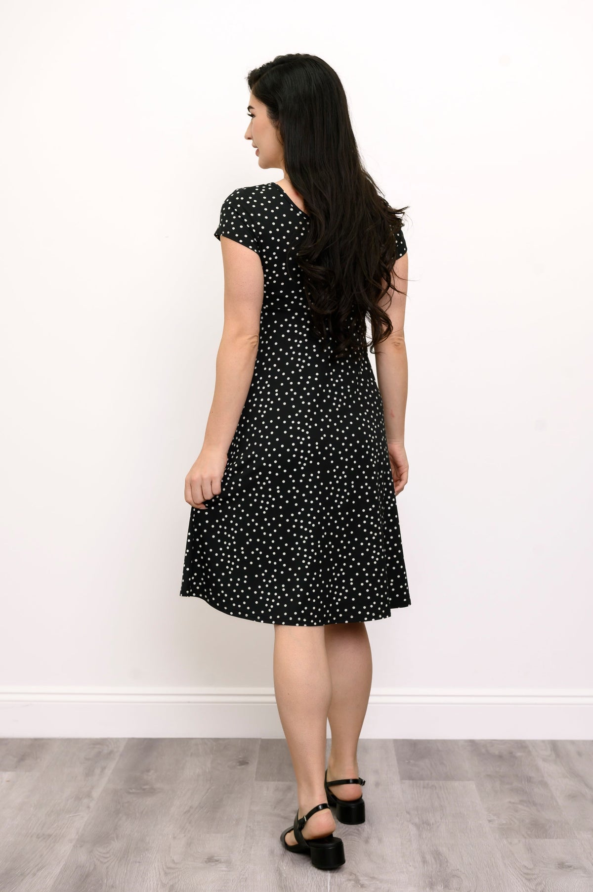 Back view of woman wearing a black dress with white polka dots on it and black shoes