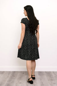 Back view of woman wearing a black dress with white polka dots on it and black shoes
