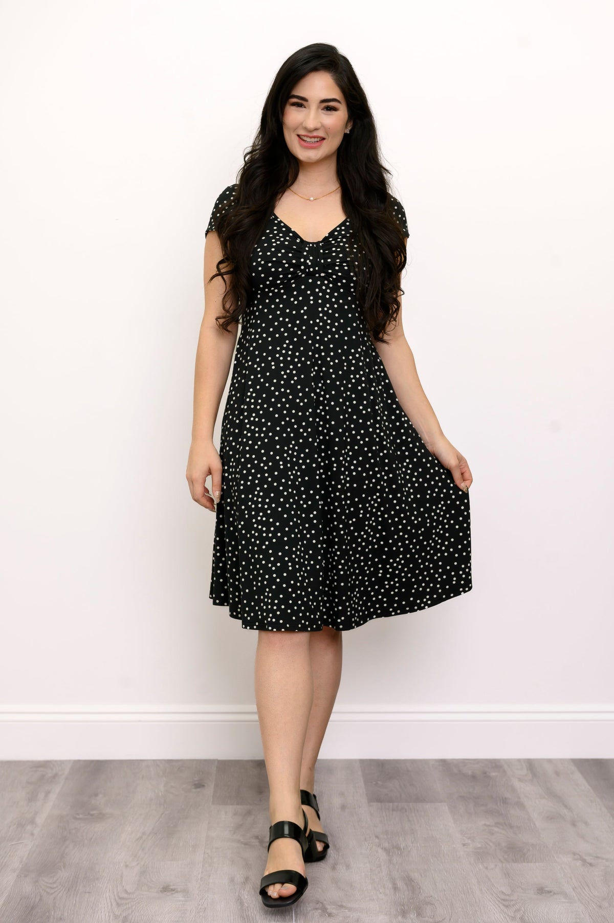woman wearing black sandals and smiling while grabbing the hem of her dress with her left hand