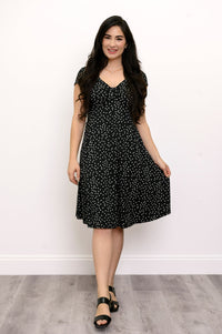woman wearing black sandals and smiling while grabbing the hem of her dress with her left hand