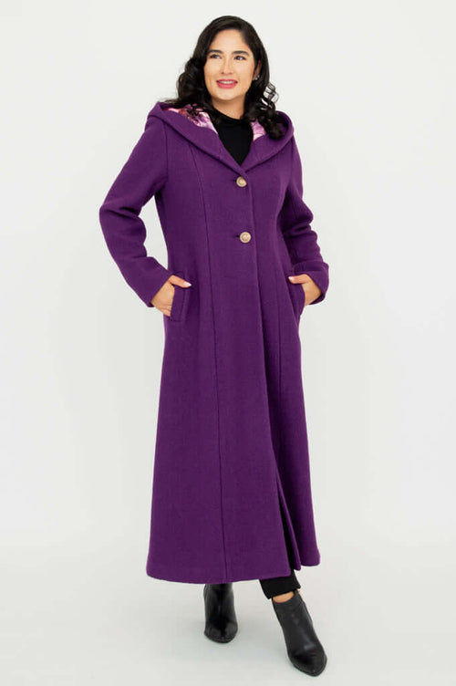 Woman wearing a long purple hooded coat with button closure, standing with hands in pockets