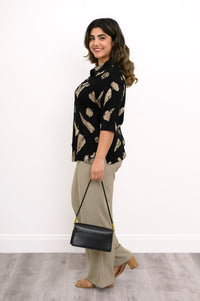 side view of woman wearing a black blouse with tan leaf pattern and beige pants styled with a black bag